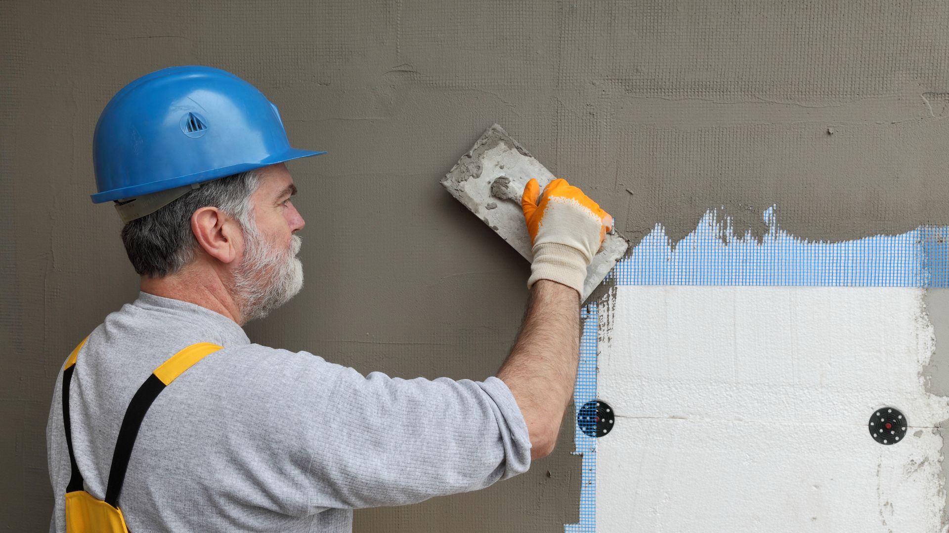 Worker spreading  mortar over styrofoam insulation and mesh  with trowel