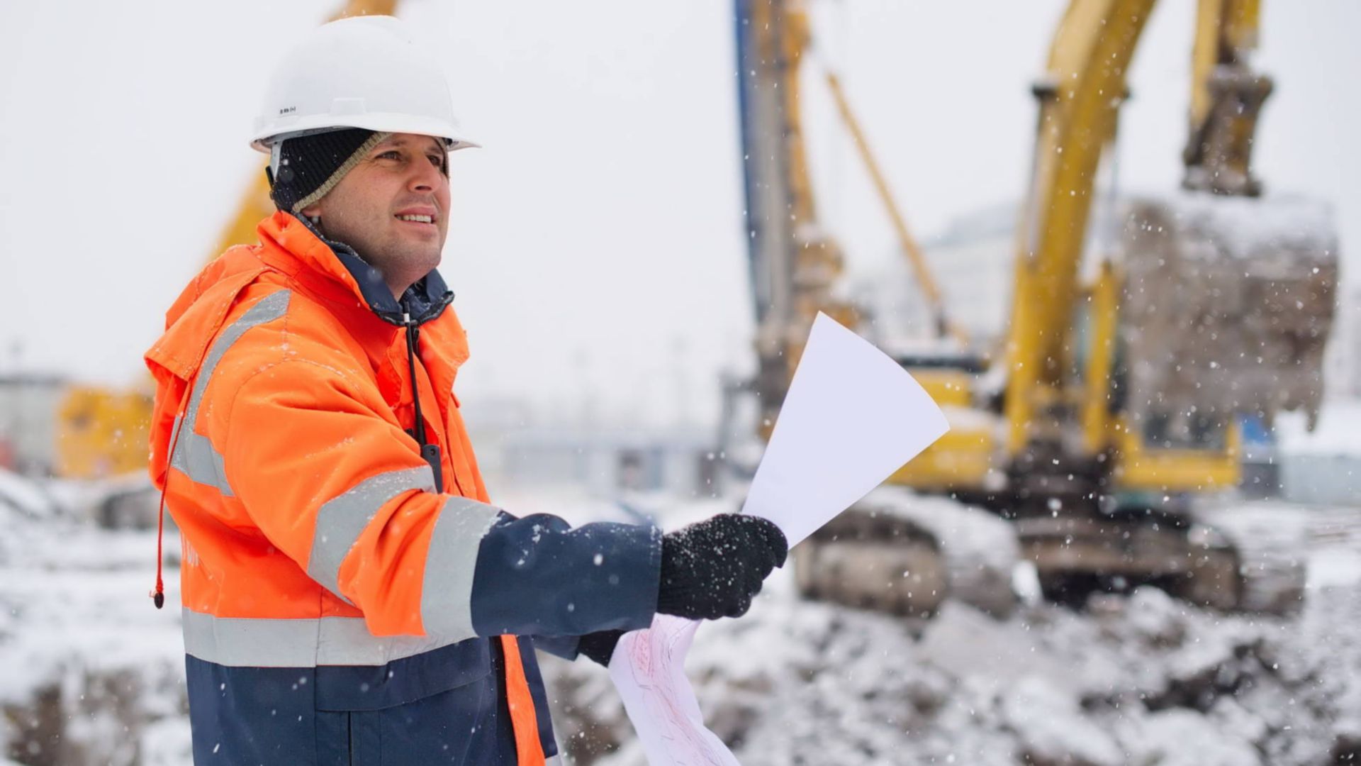 Civil engineer at construction site is inspecting ongoing works according to design drawings in difficult winter conditions