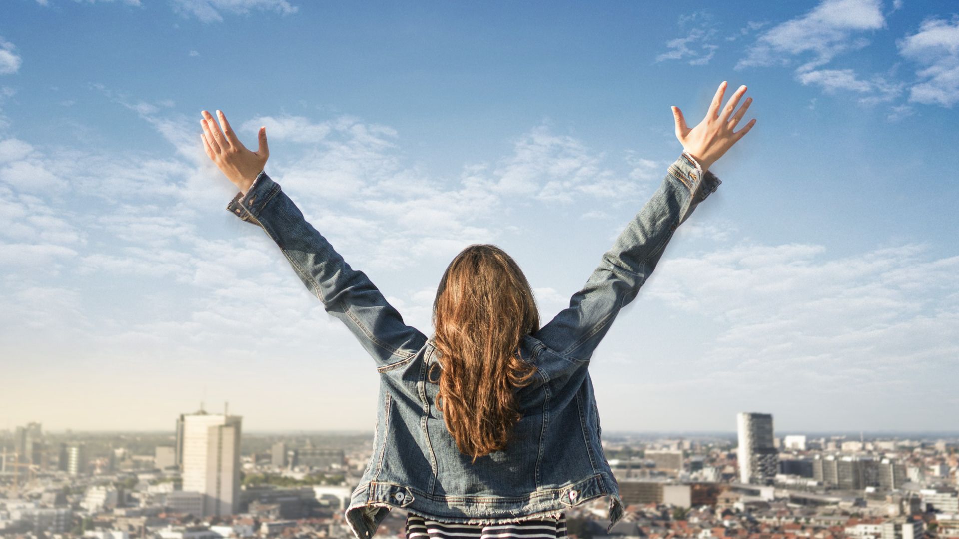 Woman standing on a rooftop with arms wide open, having a whole city under her foot.