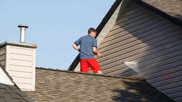 Man standing on the roof of his house cleaning the siding.