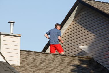 站立在他的房子的屋顶的人清洗壁橱的。