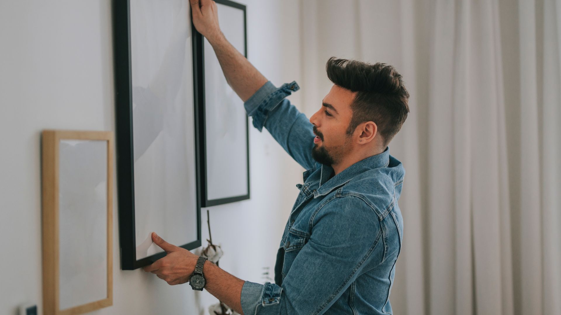 a middle eastern man with beard hanging a painting on the wall at his living room