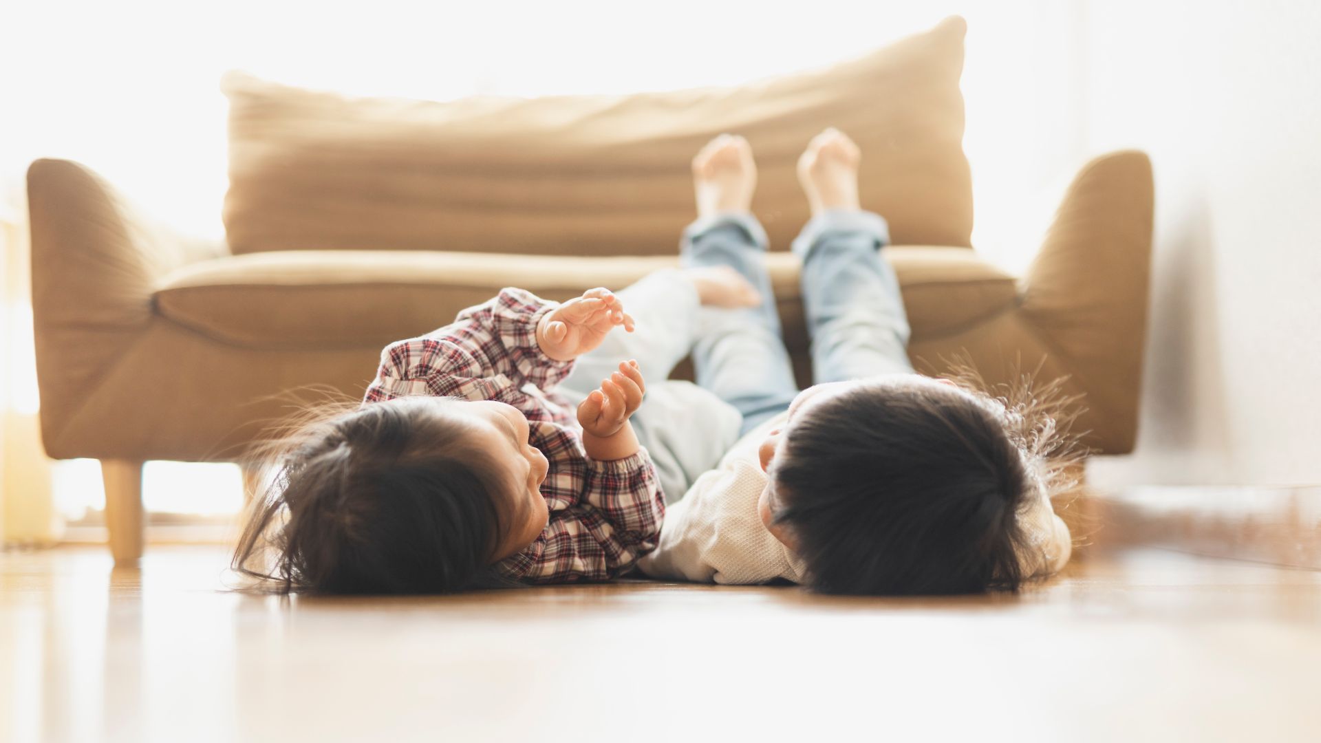 Asian older brother and younger sister lying down on floor in the living room.