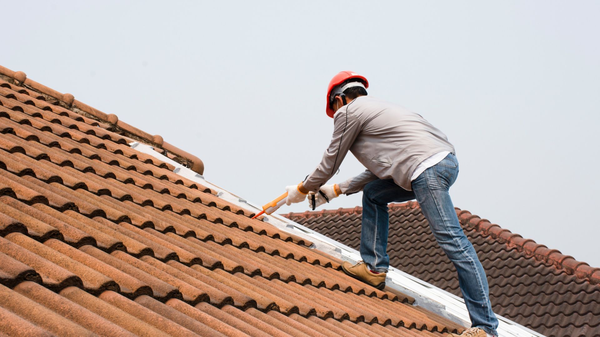 Technician man hand using glue gun with silicone adhesive or manual caulking gun with polyurethane to seal the leakage on the roof. Installing and building construction concept.