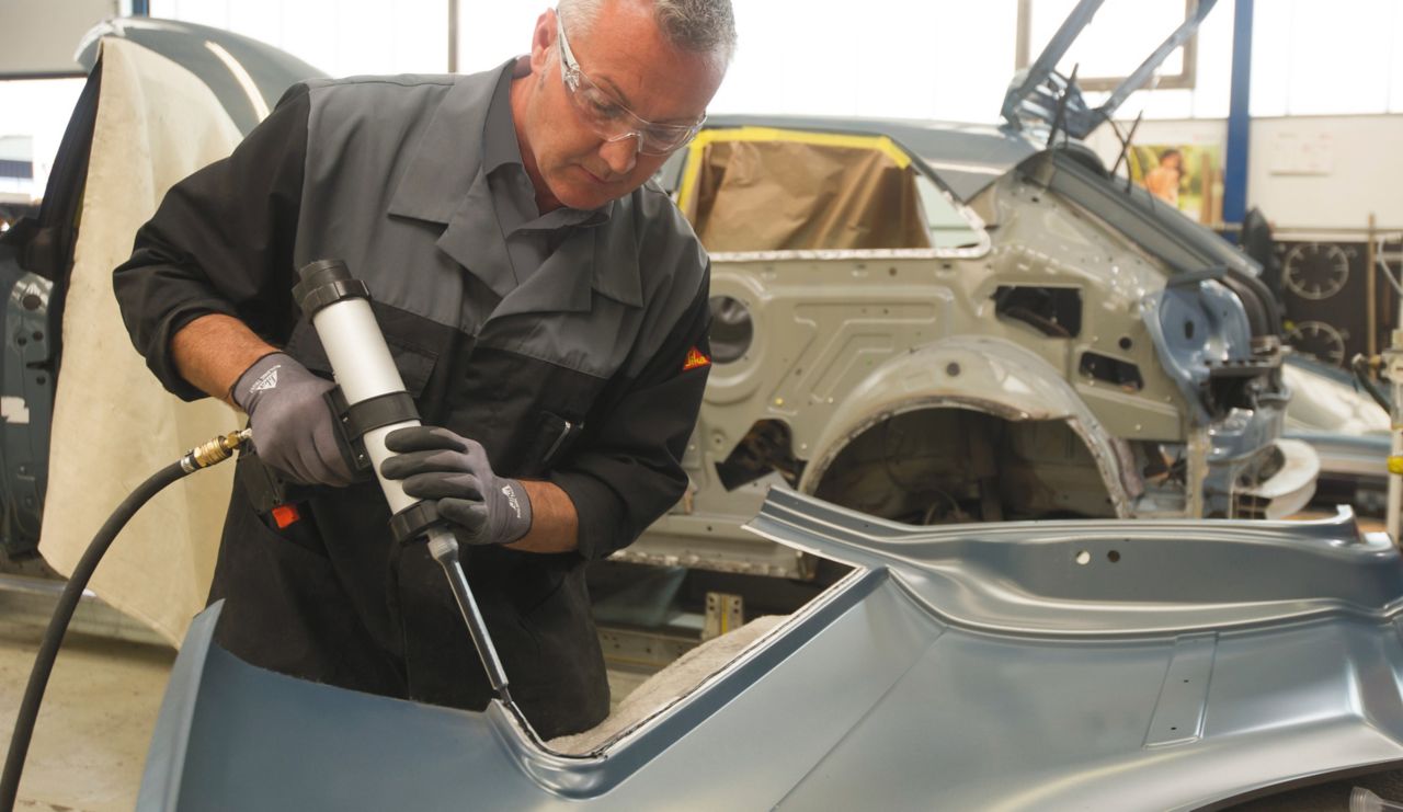 自動車修理工場でシーカの接着剤を使って車体修理する男性