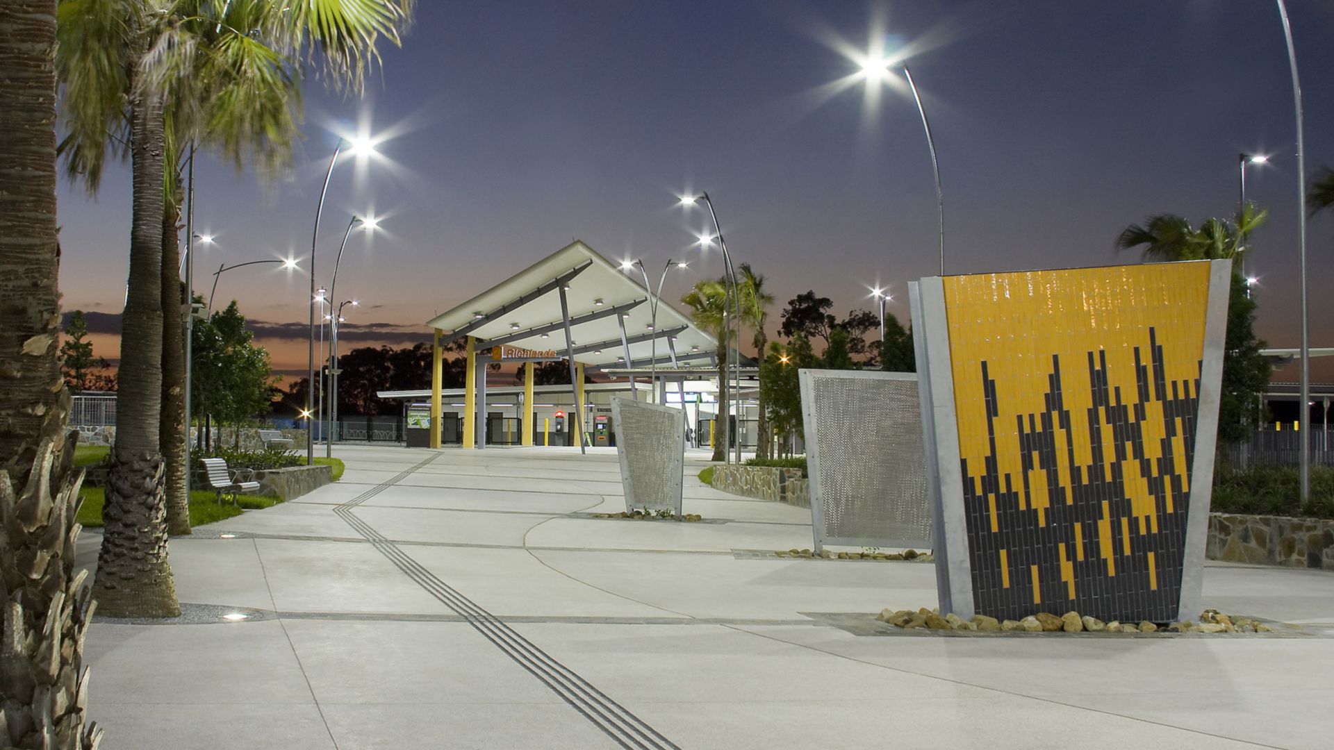 Smooth finished concrete sidewalk at transport station in Brisbane, Australia with guides for blind, palm trees and yellow tiled sculpture