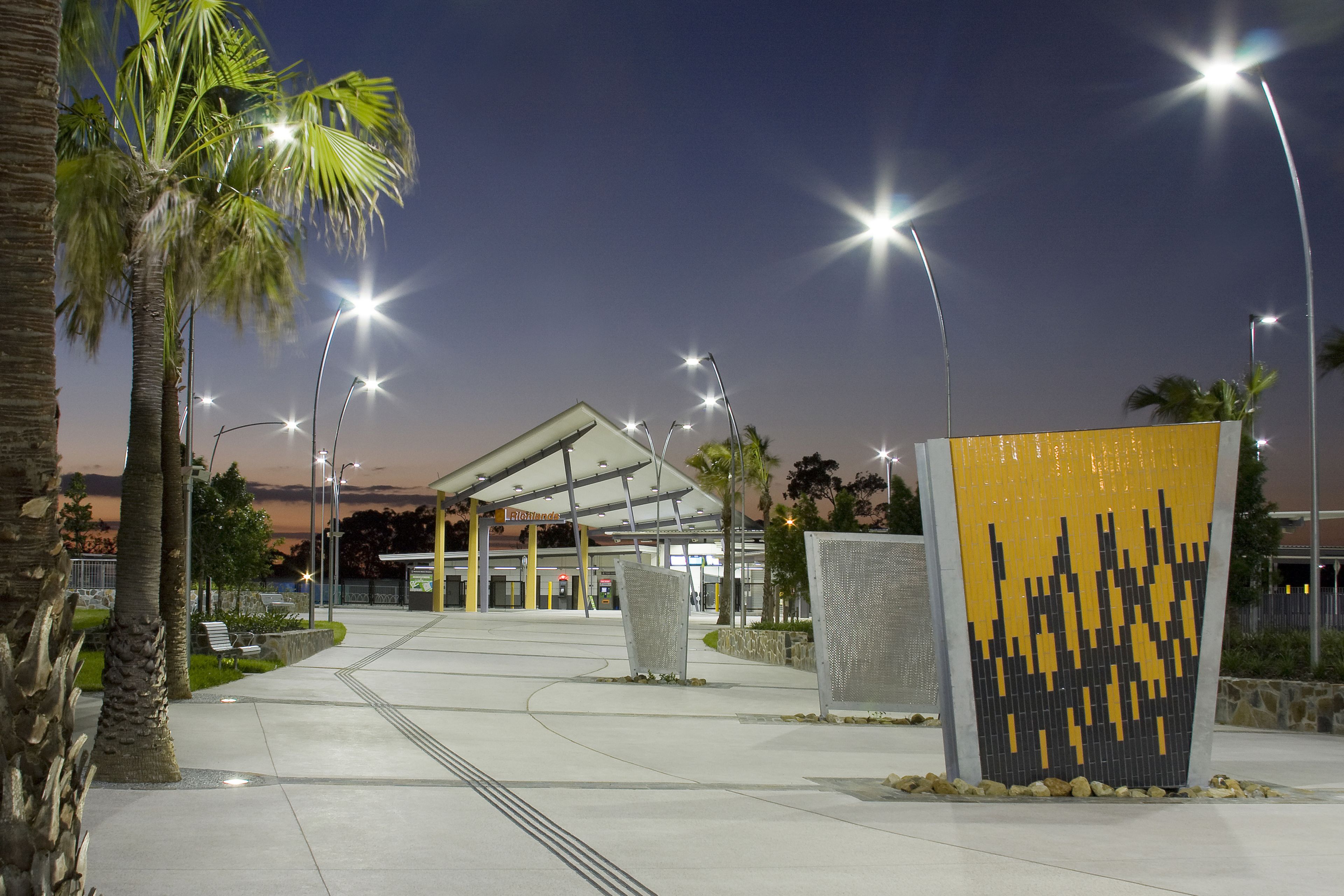 Smooth finished concrete sidewalk at transport station in Brisbane, Australia with guides for blind, palm trees and yellow tiled sculpture