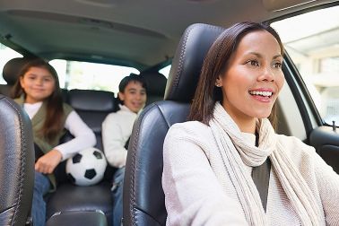 Mother driving in automobile with daughter and son in back seat