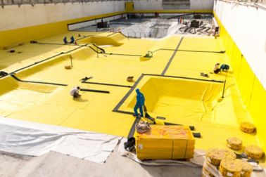    Construction workers applying a below-grade waterproofing membrane	 