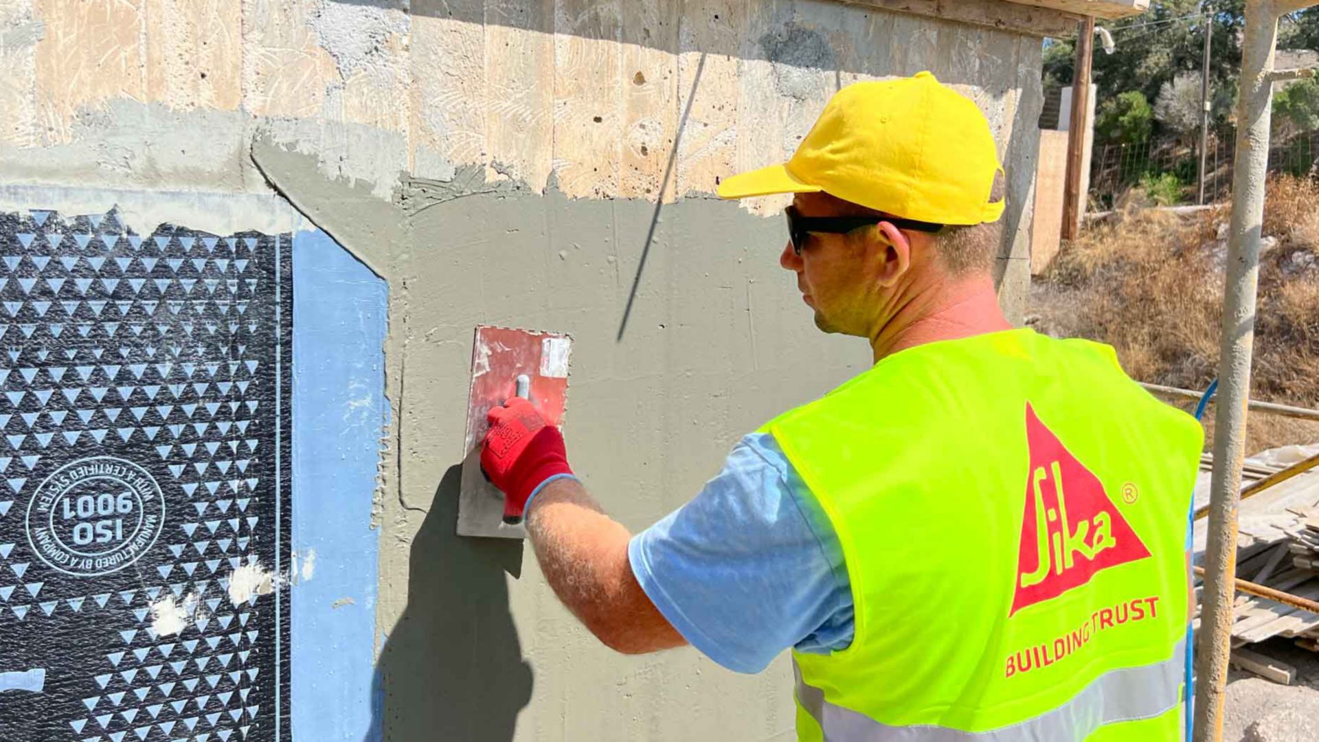 Man applying cement adhesive for SikaShield® bitumen waterproofing membrane on wall