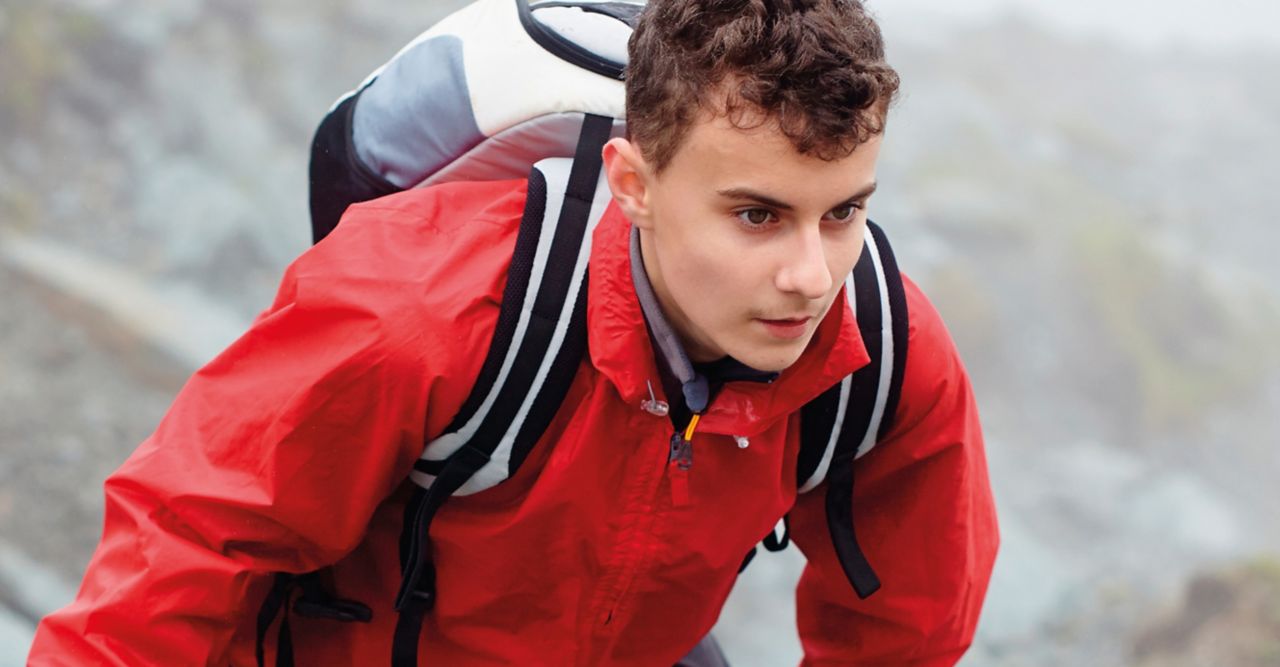 Young man climbing up a mounted in a laminted red jacket