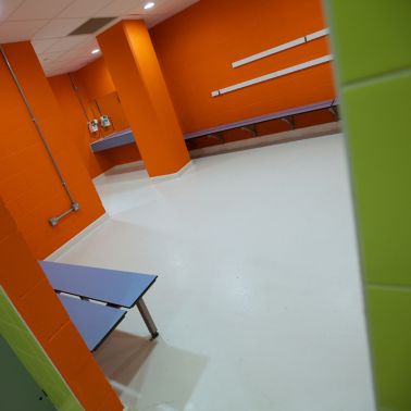 Sika ComfortFloor® white floor with orange and green walls in sport center bathroom changing room