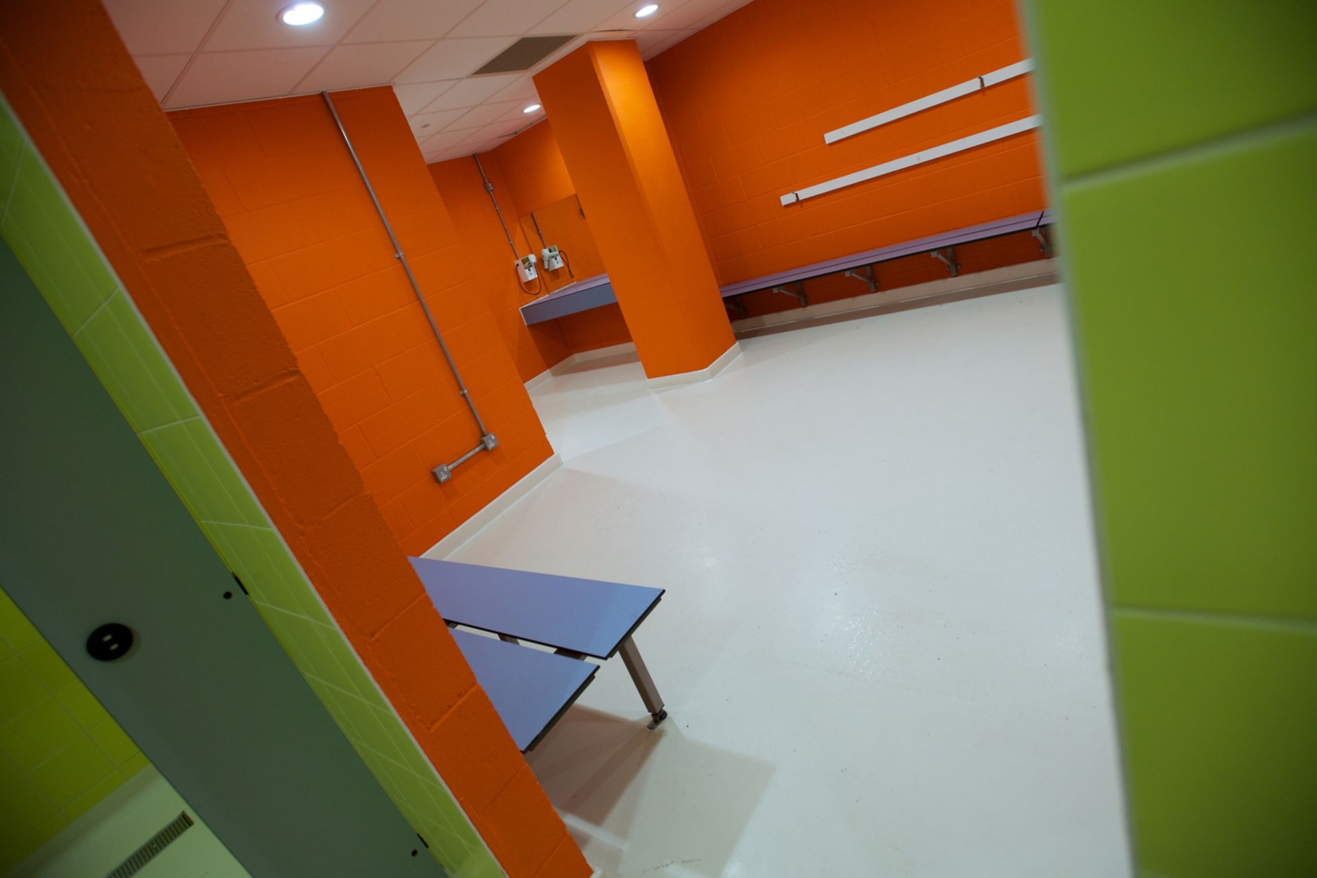 Sika ComfortFloor® white floor with orange and green walls in sport center bathroom changing room