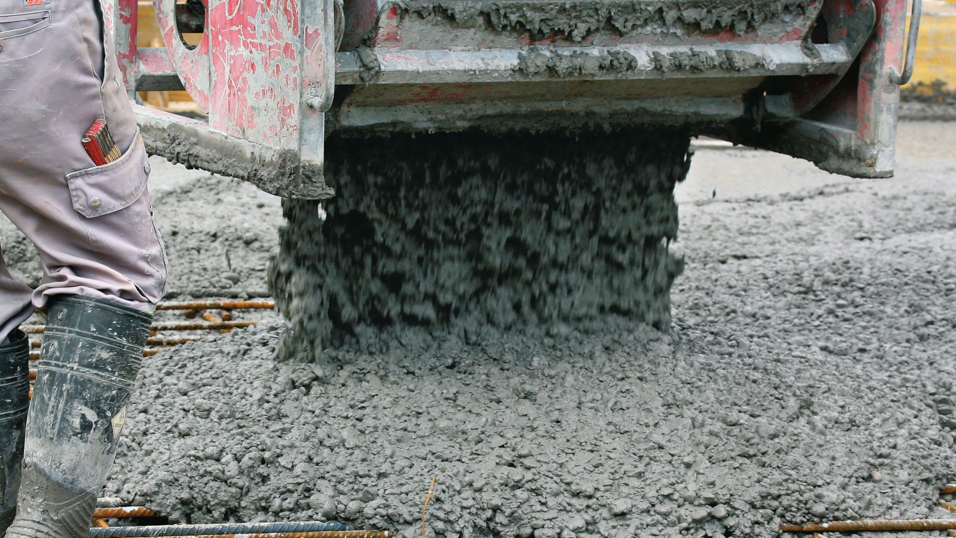 Worker in boots pouring concrete over rebar