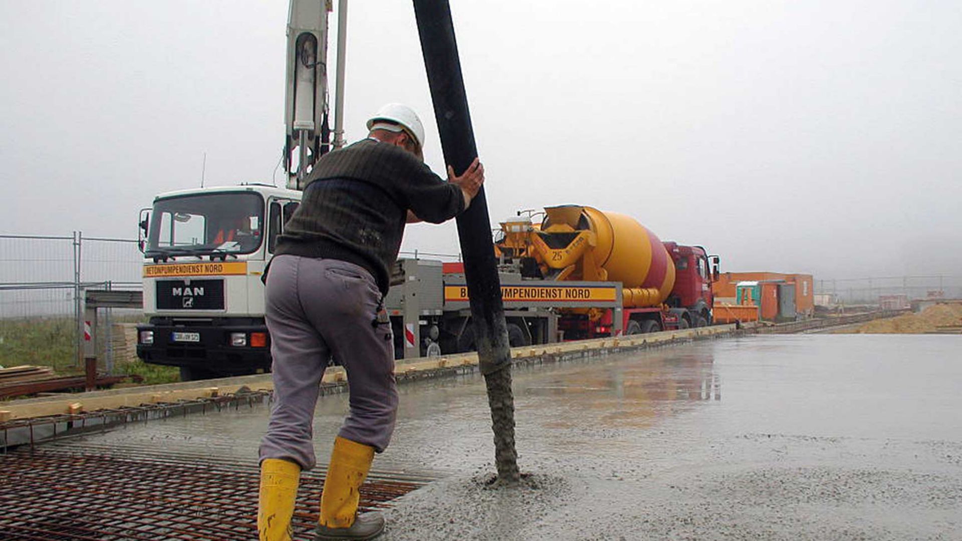 Worker in boots pouring concrete out of truck pump pipe over rebar for concrete slab