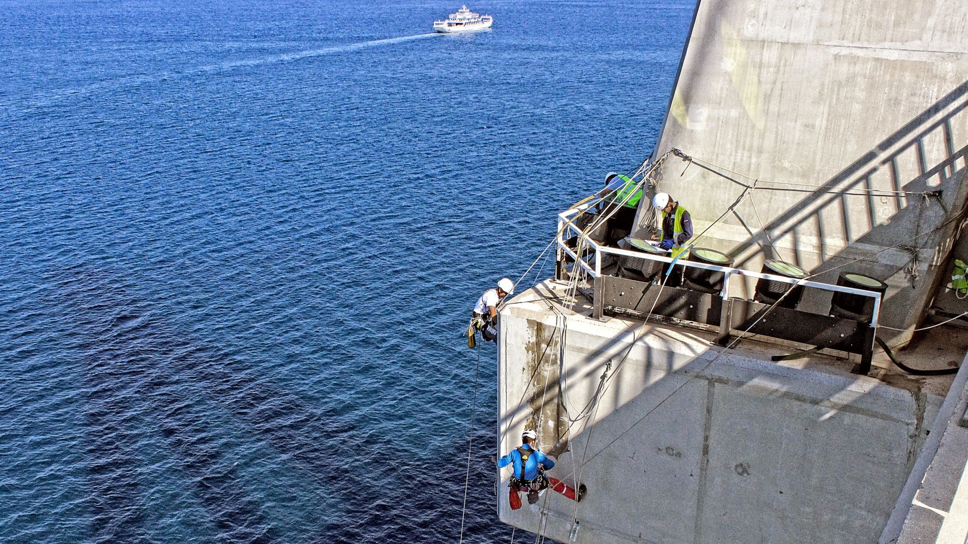   Man repairing a concrete bridge, hanging over the sea	 