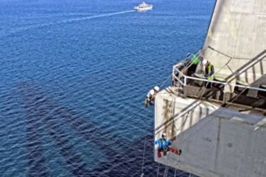   Man repairing a concrete bridge, hanging over the sea	 