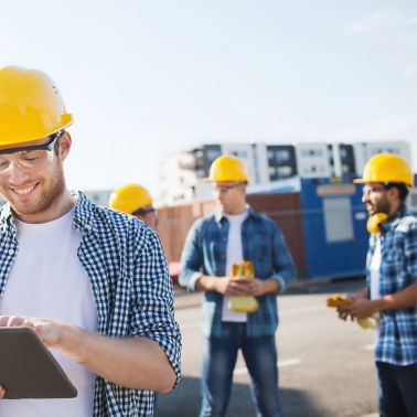 Group of smiling builders men in hardhats with tablet outdoors on construction site
