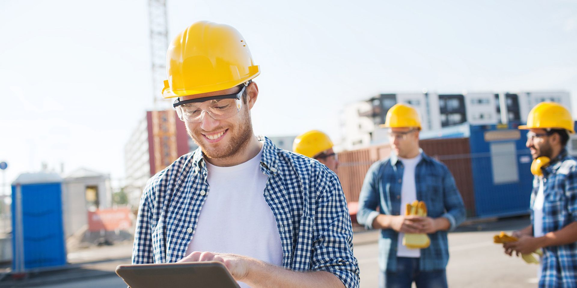 Group of smiling builders men in hardhats with tablet outdoors on construction site