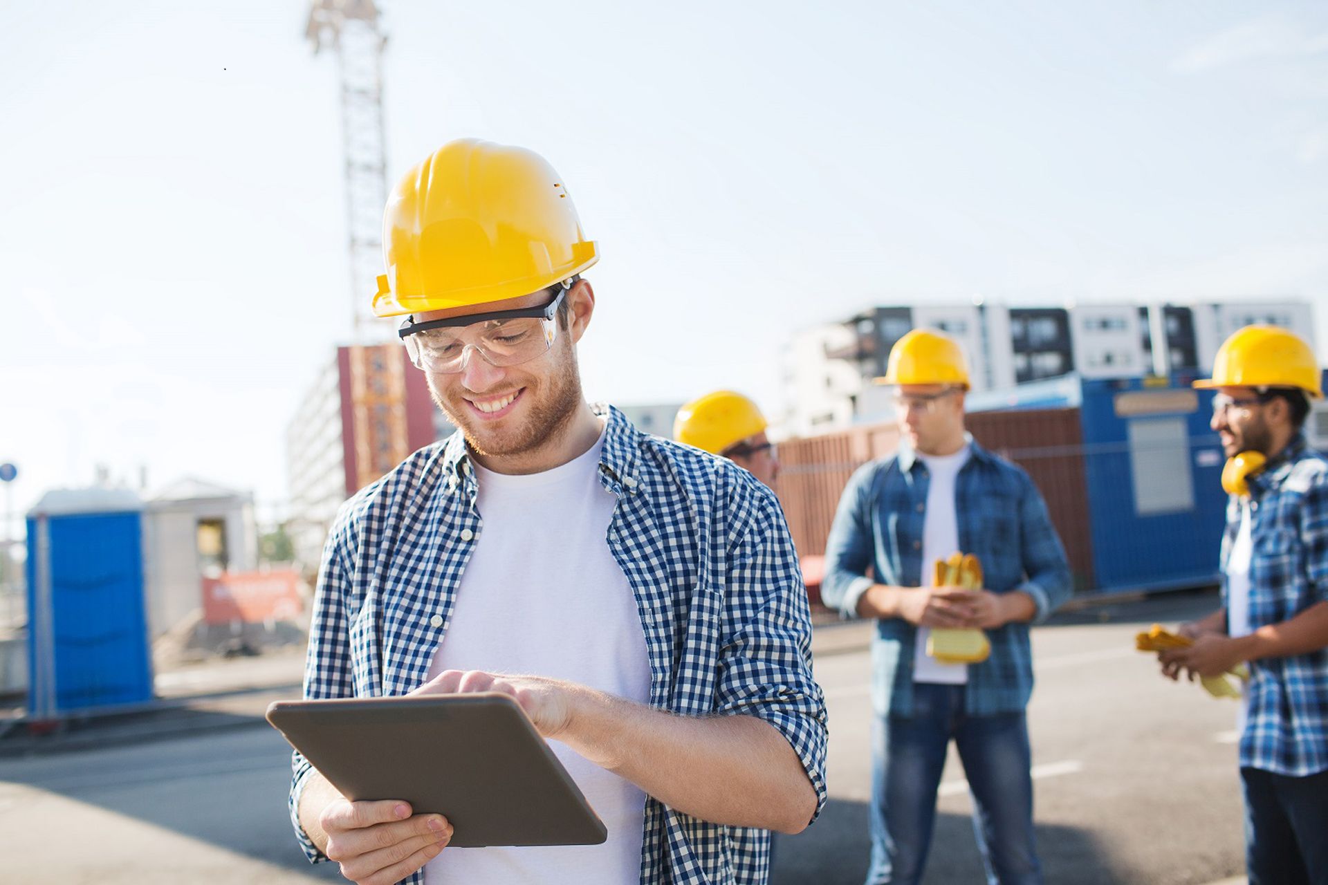 Group of smiling builders men in hardhats with tablet outdoors on construction site