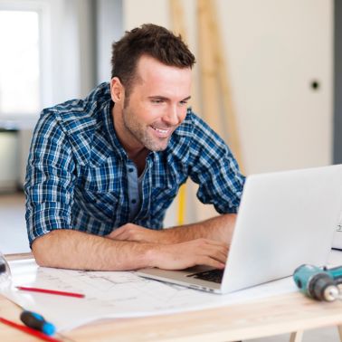 微笑的DIY建筑工人人与膝上型计算机一起使用