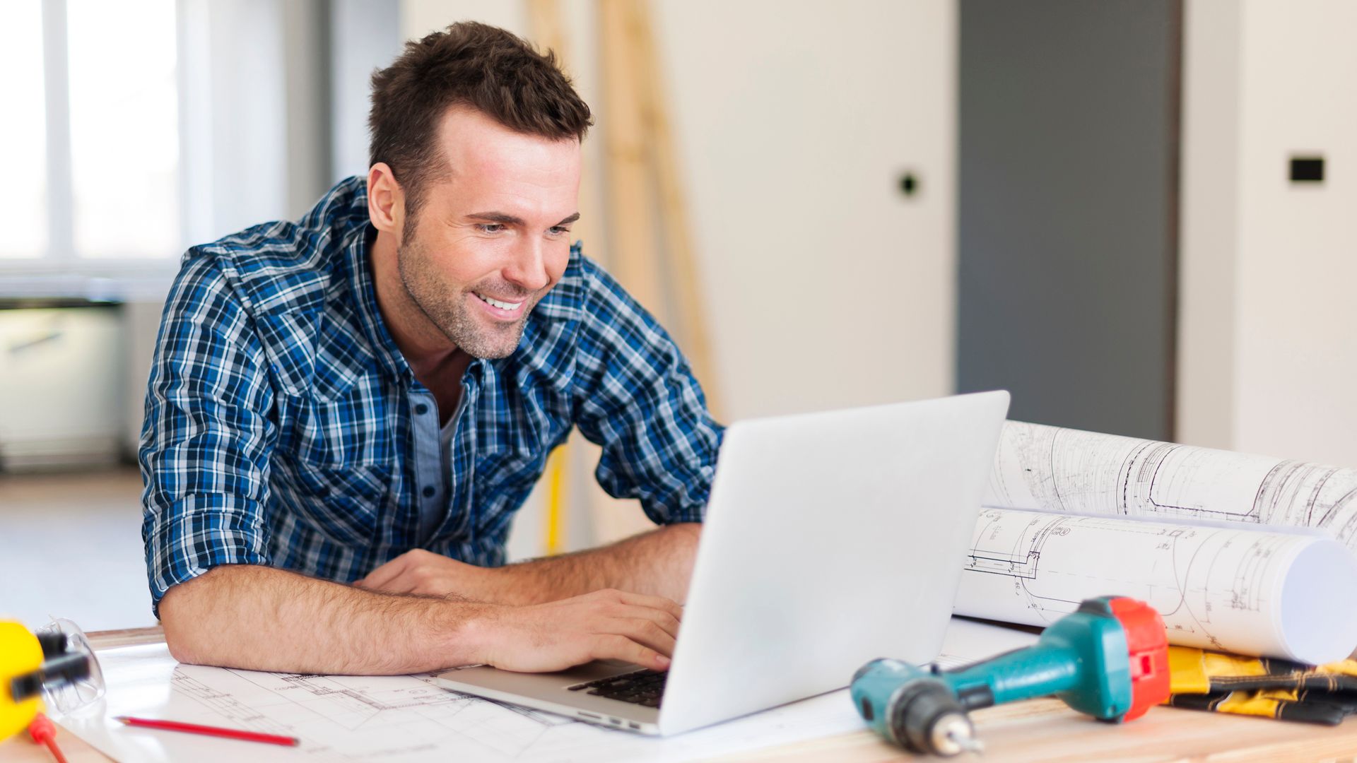 Smiling DIY construction worker man working with laptop 