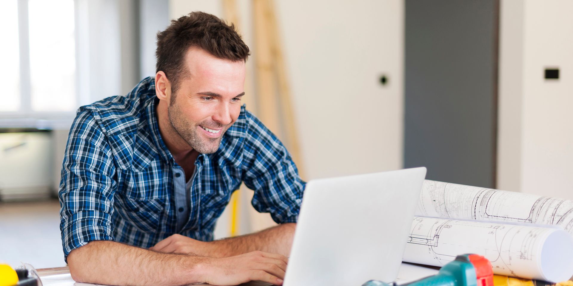 Smiling DIY construction worker man working with laptop 