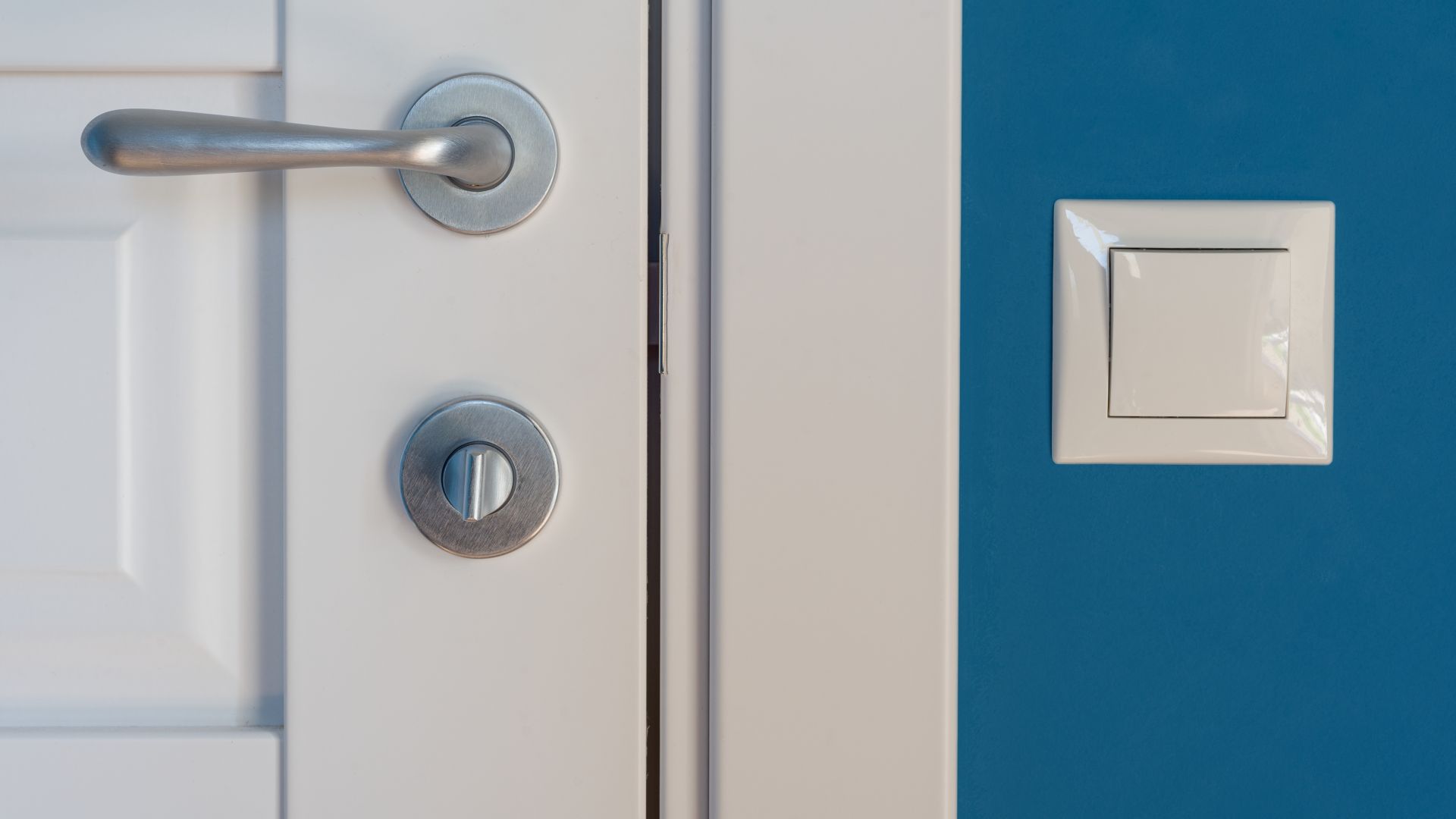 Close-up elements of the interior of the apartment. Detail of a white interior door with a chrome door handle and latch, light switch on the wall.