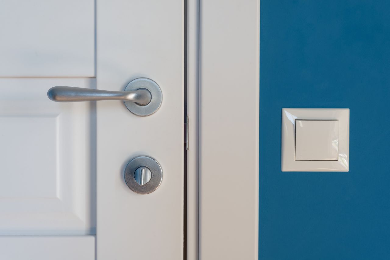Close-up elements of the interior of the apartment. Detail of a white interior door with a chrome door handle and latch, light switch on the wall.