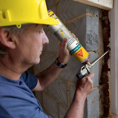 男人在窗口和墙壁之间应用锡卡蓬勃发展泡沫