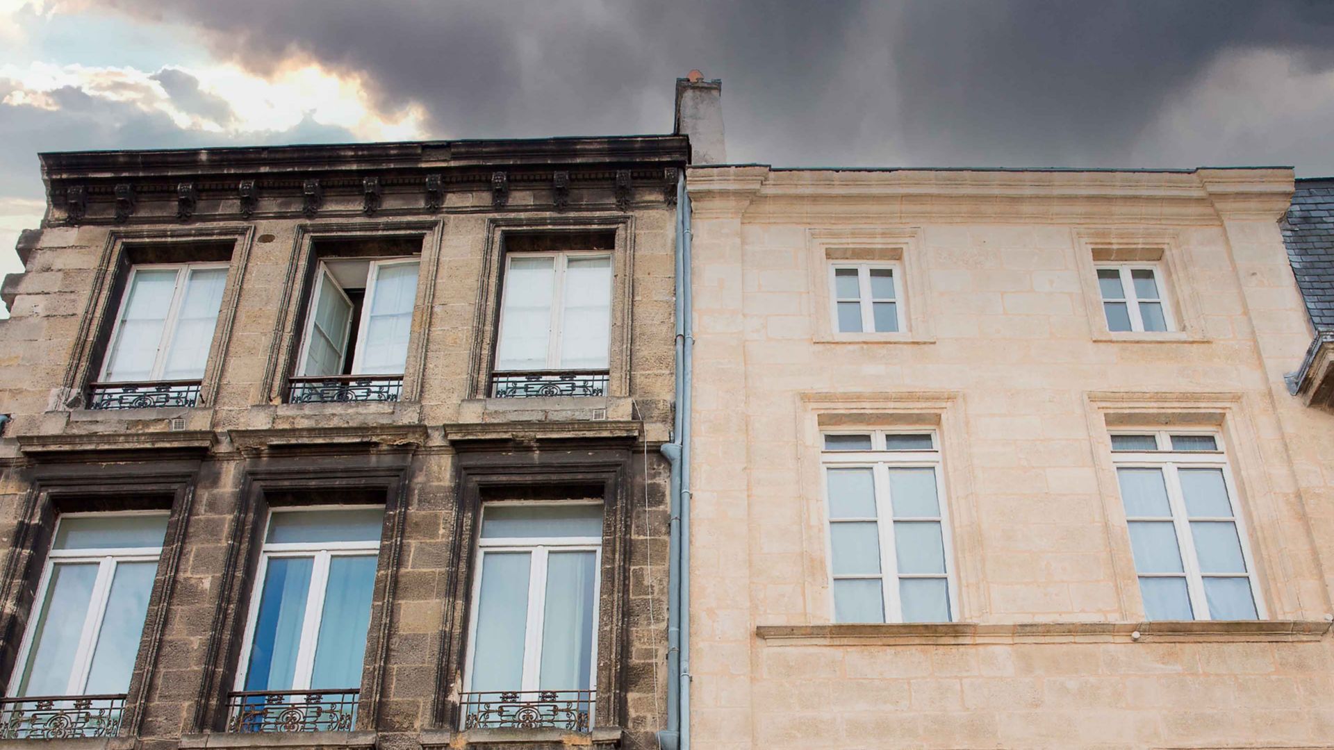 Stone house facade dirty brown stone vs. clean white stone after Sika cleaning products with stormy sky