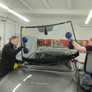 Two fitter placing windshield into frame of a car