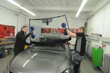 Two fitter placing windshield into frame of a car