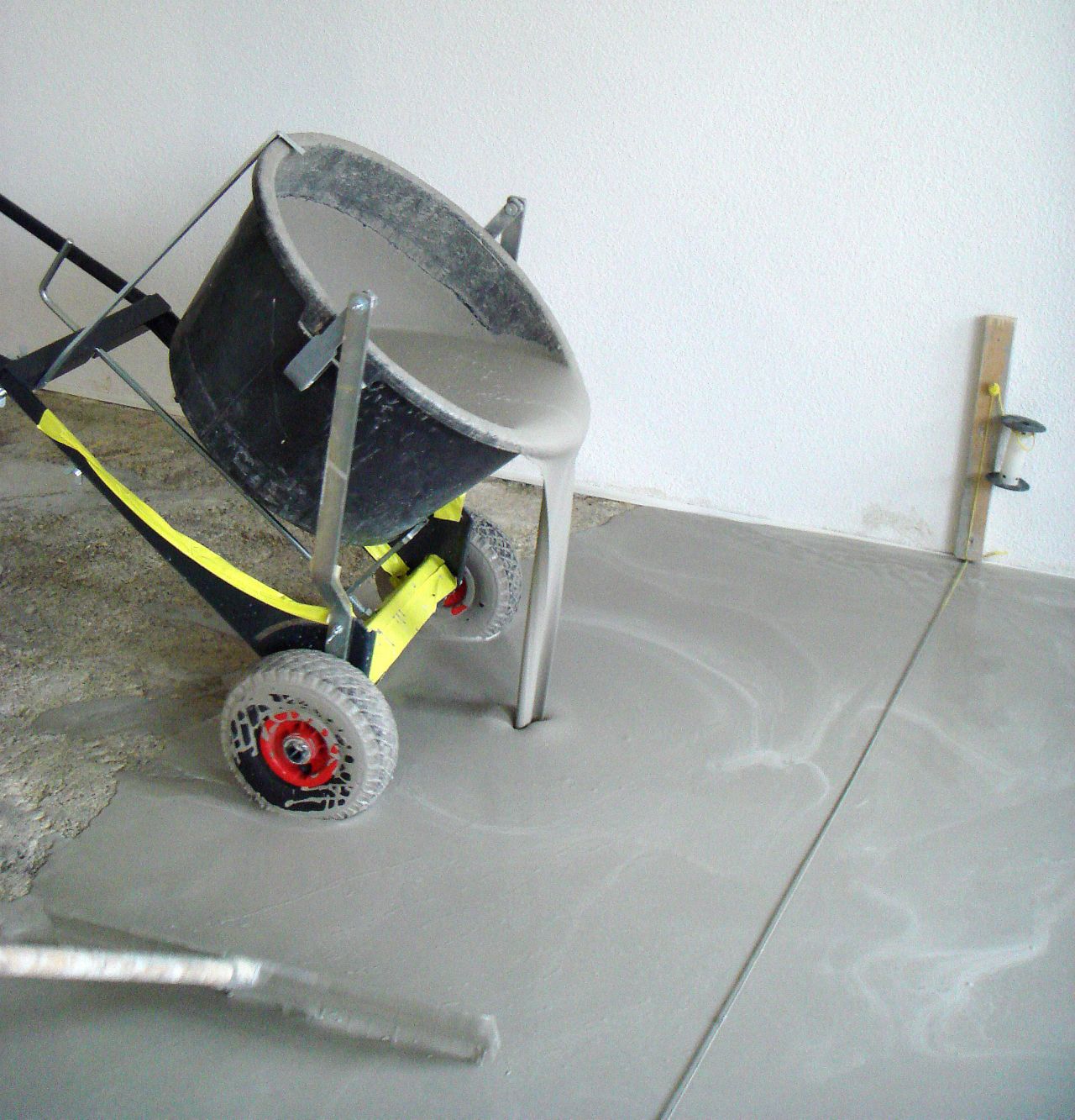 Sika applicator applying floor leveling from yellow bucket to shiny floor