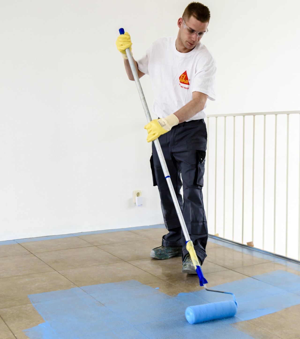 Sika applicator applying blue primer coat to floor tiles