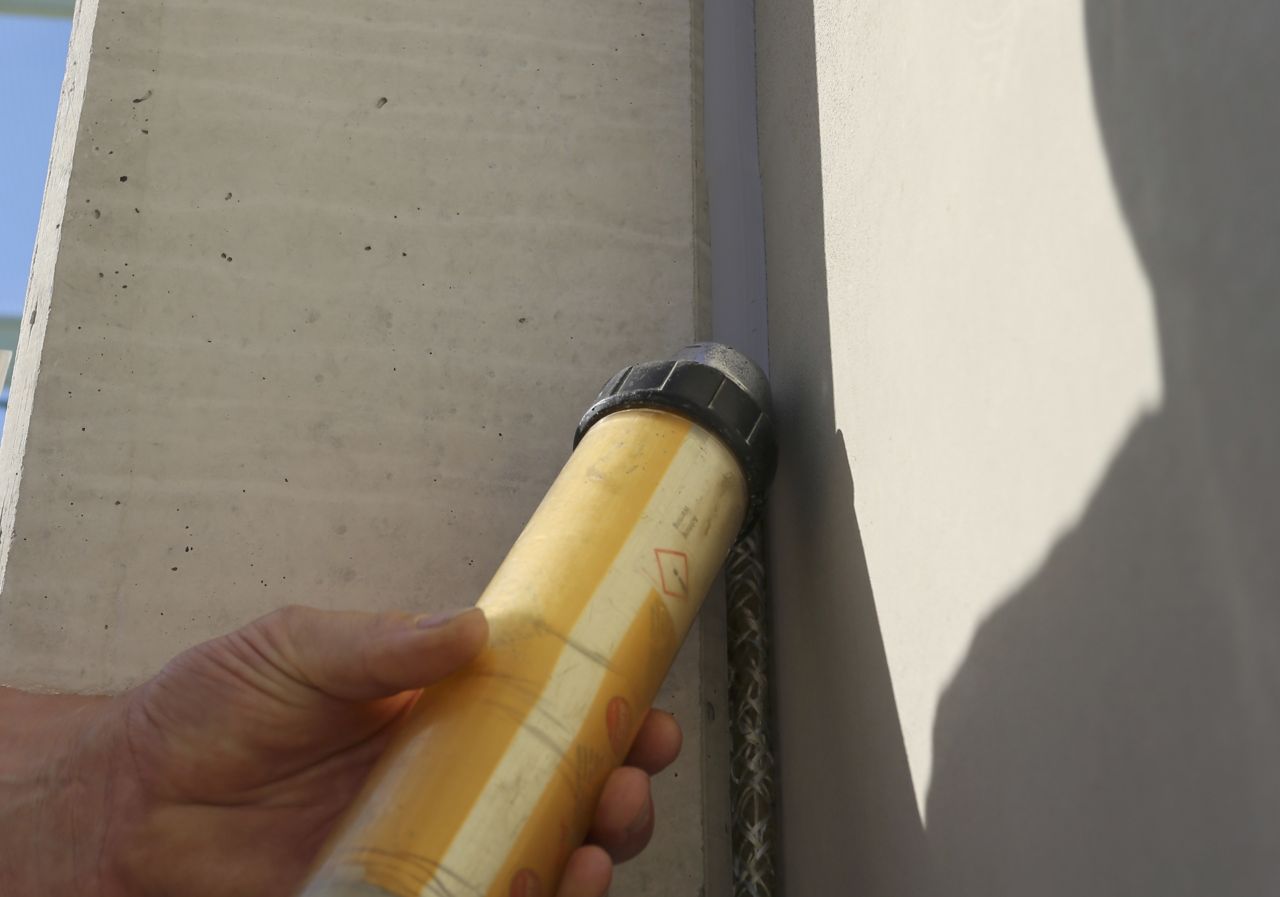 Hand applying joint sealant to concrete building with Sikaflex cartridge