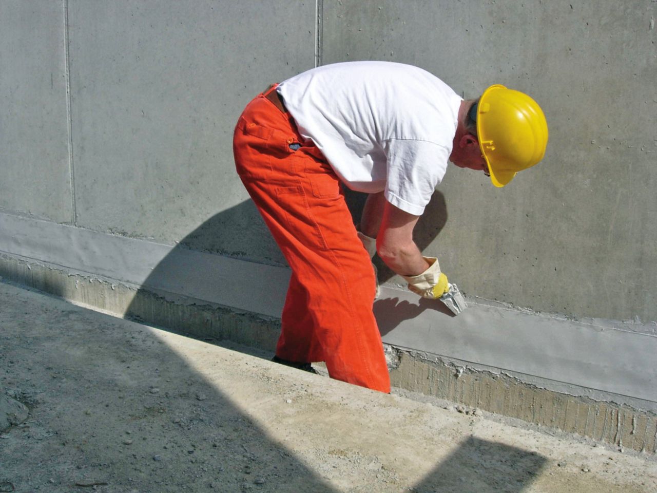 Male applicator applying Sikadur Combiflex to joint in concrete facade of building with hand trowel