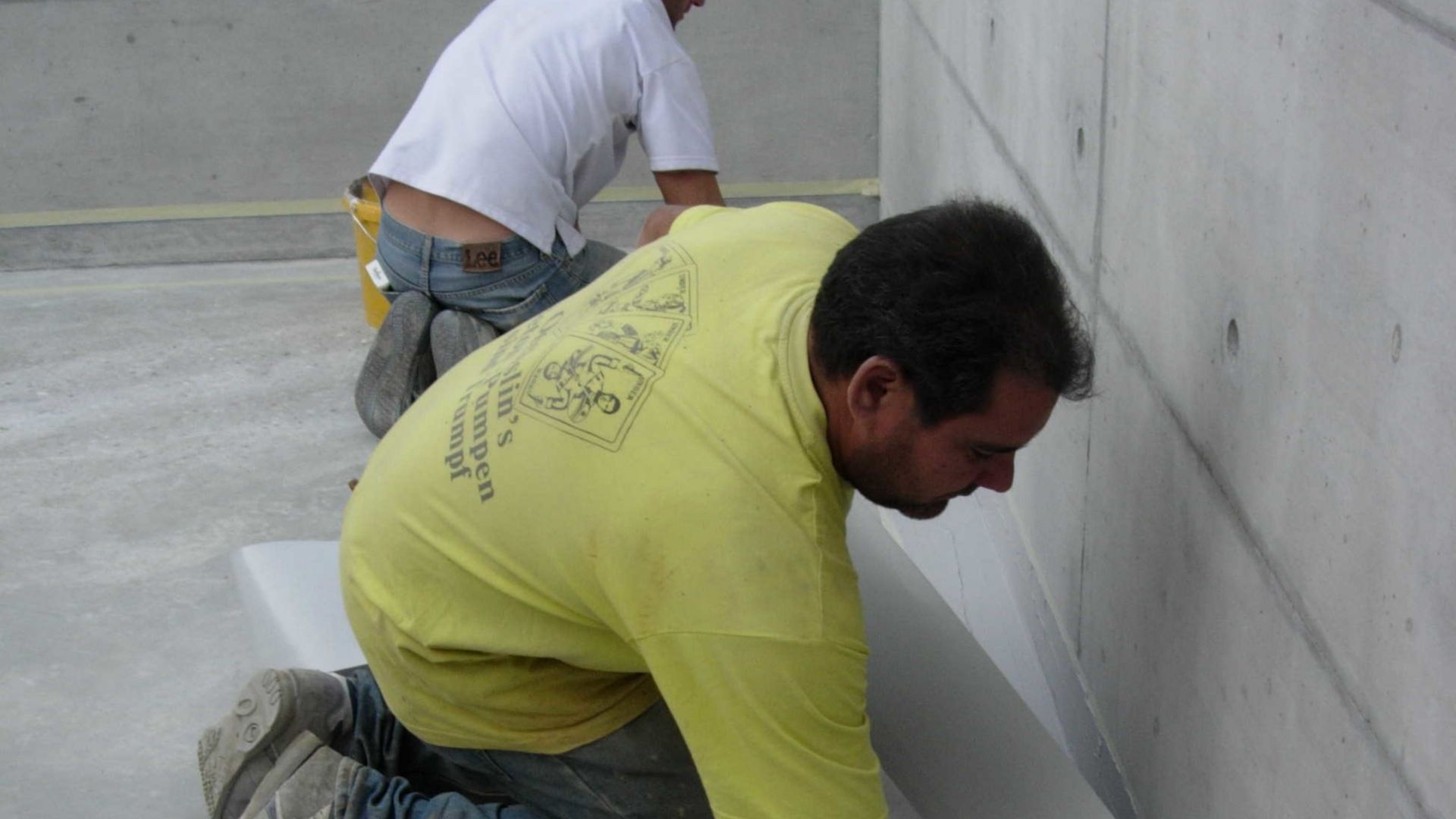 Male applicators applying Sikadur Combiflex waterproofing tape to concrete joint in building by hand