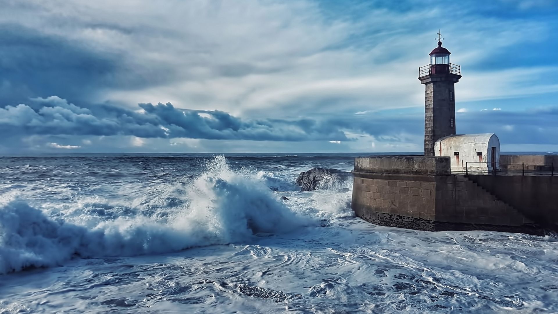 Lighthouse at sea with waves crashing and clouds