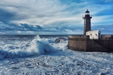 Lighthouse at sea with waves crashing and clouds