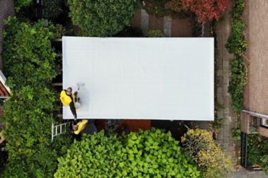 Construction workers applying Sikalastic-580 liquid applied membrane on the roof drone view