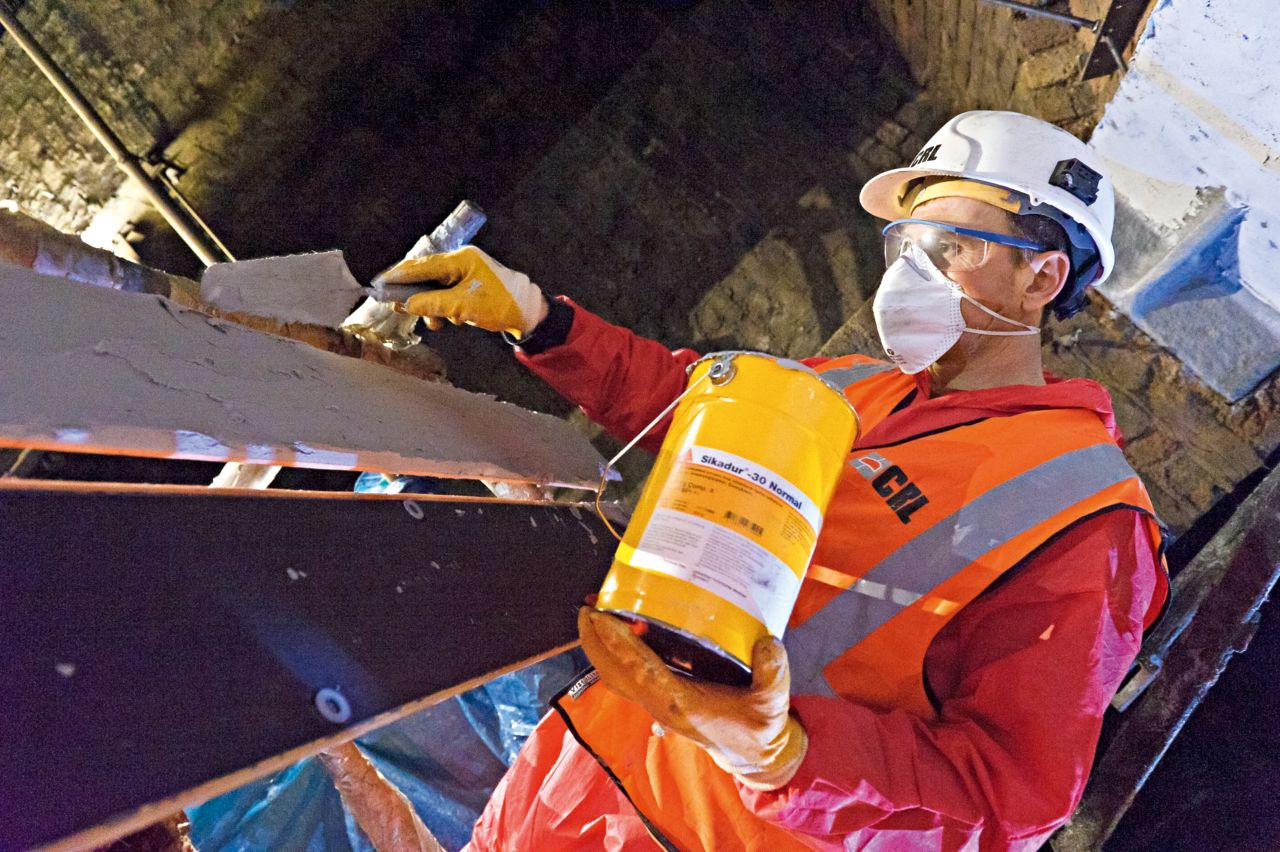 Construction worker applies epoxy adhesive on cast-iron beams