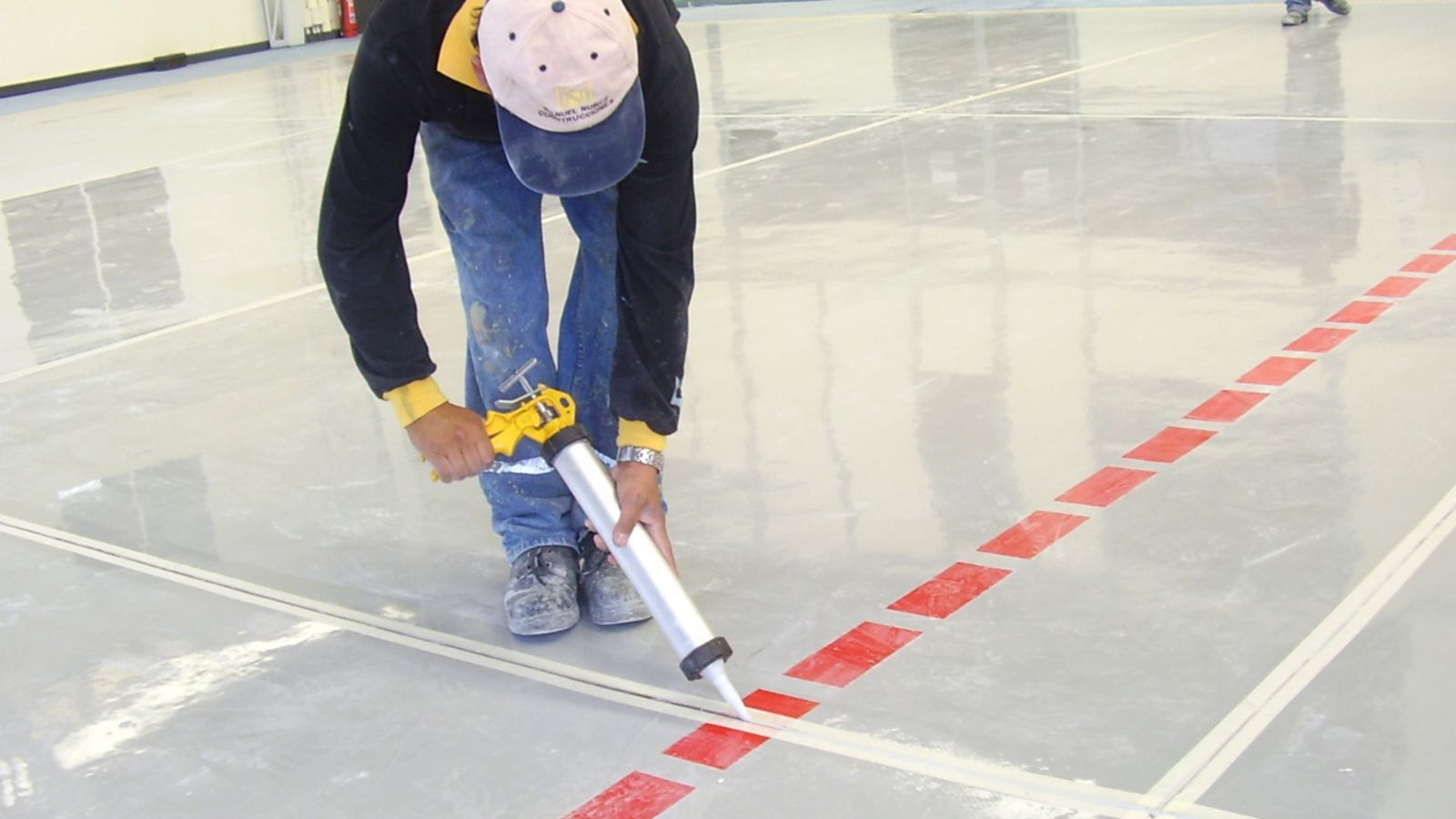 Man applying joint sealant to floor joint with hand applicator gun