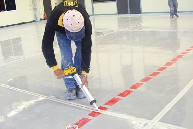 Man applying joint sealant to floor joint with hand applicator gun