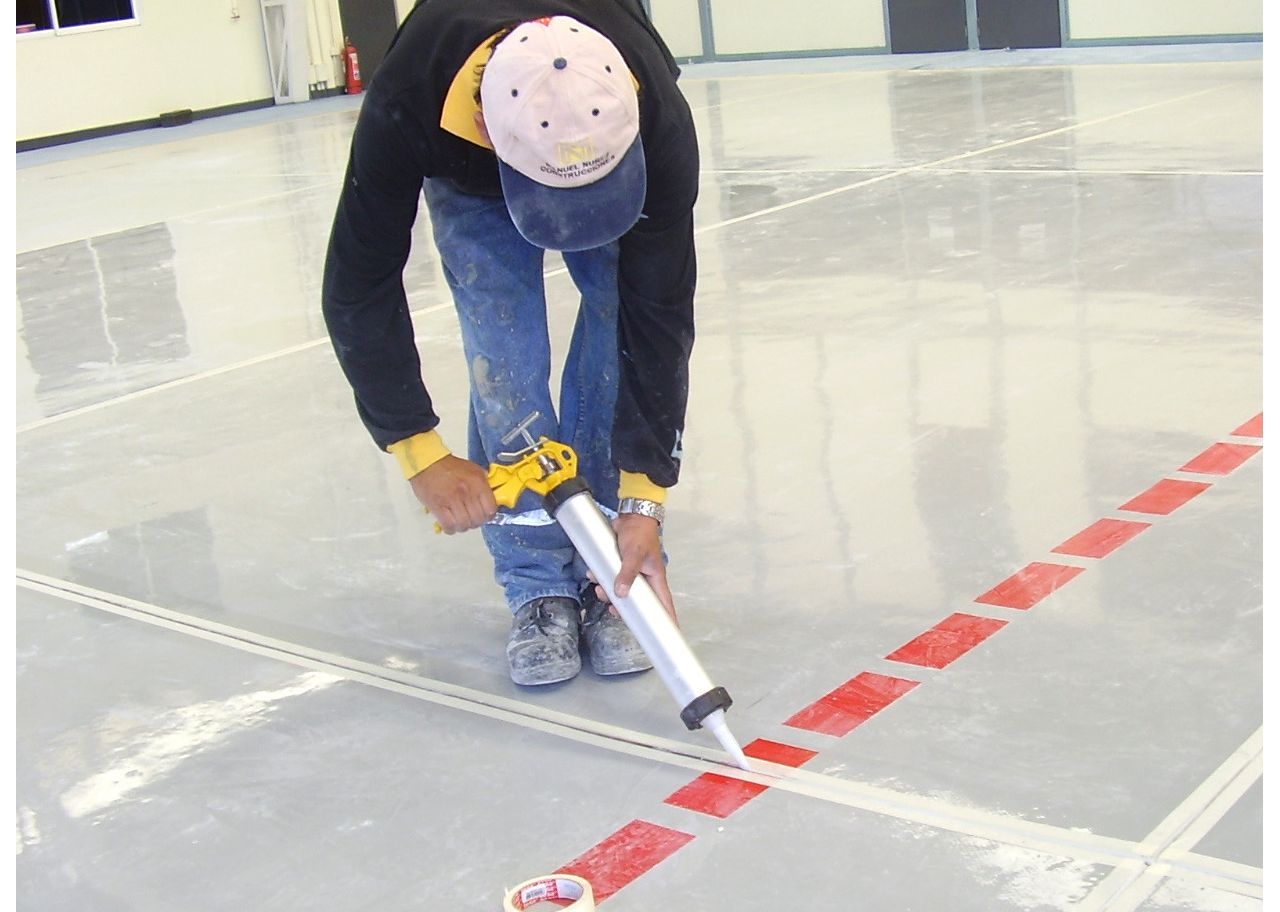 Man applying joint sealant to floor joint with hand applicator gun