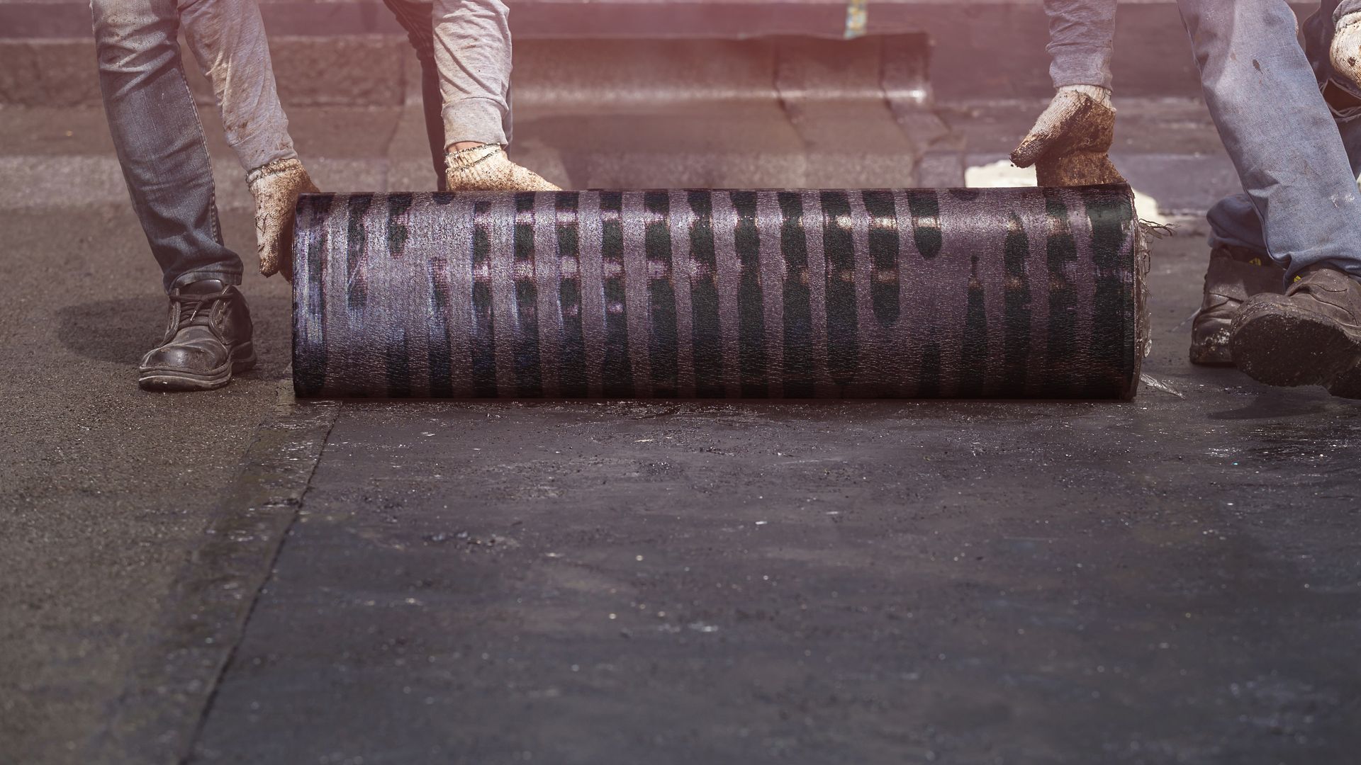 Two workers rolling SikaBit bitumen membrane apply on roof