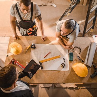 Worker men gathered around table with tablet and blueprint