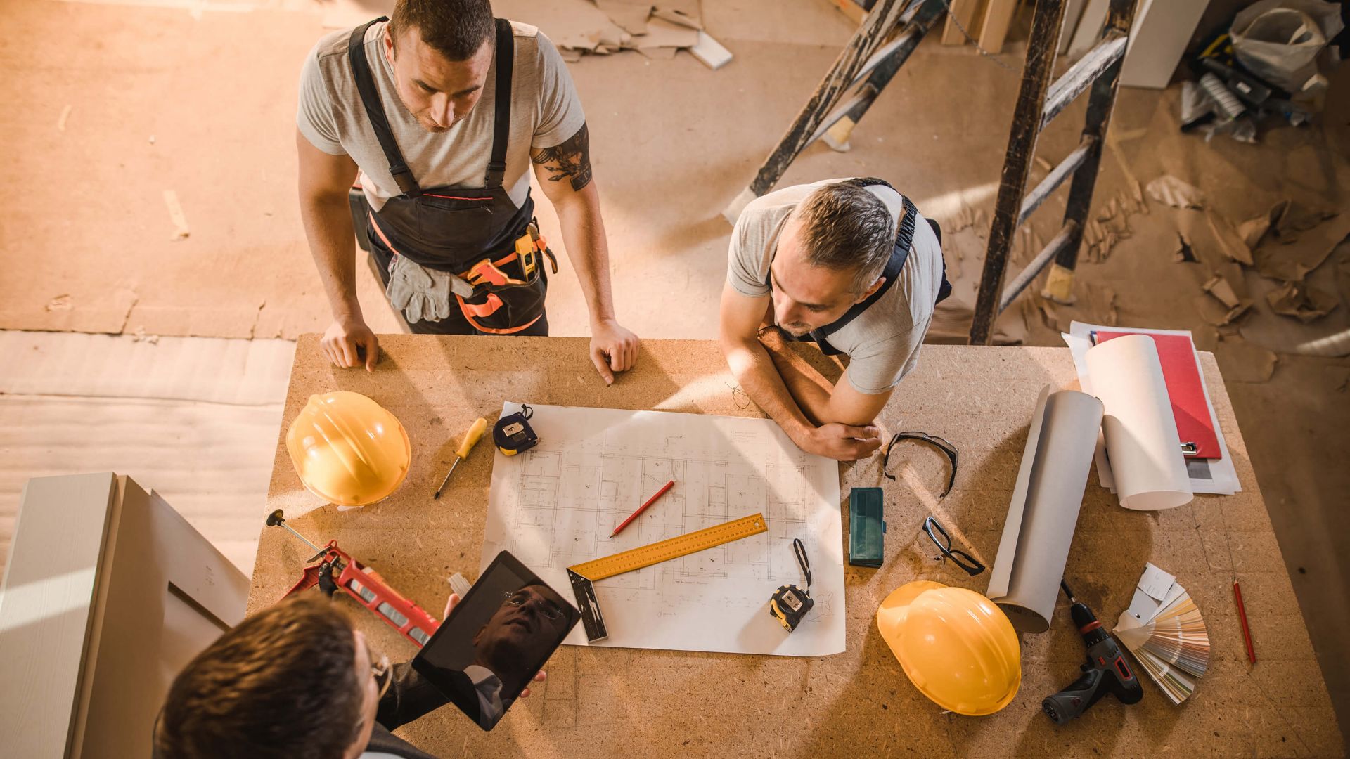 Worker men gathered around table with tablet and blueprint