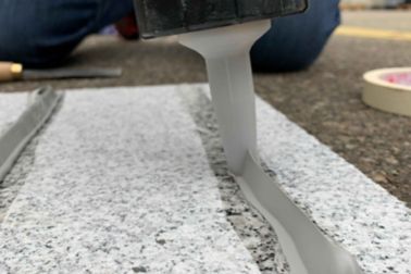 Person applying Sika Purform grey polyurethane sealant on stone surface