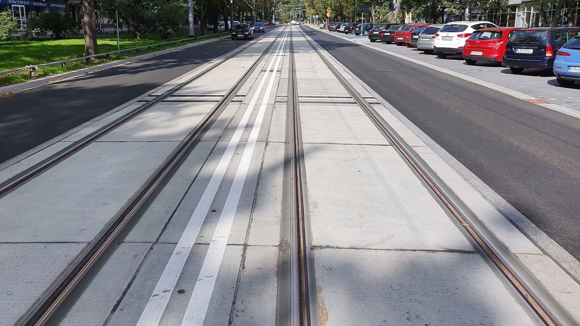 Tram rail track in street with parked cars and cars driving by and trees